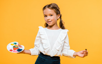 A girl in a white shirt holding a paint palette and a paint brush